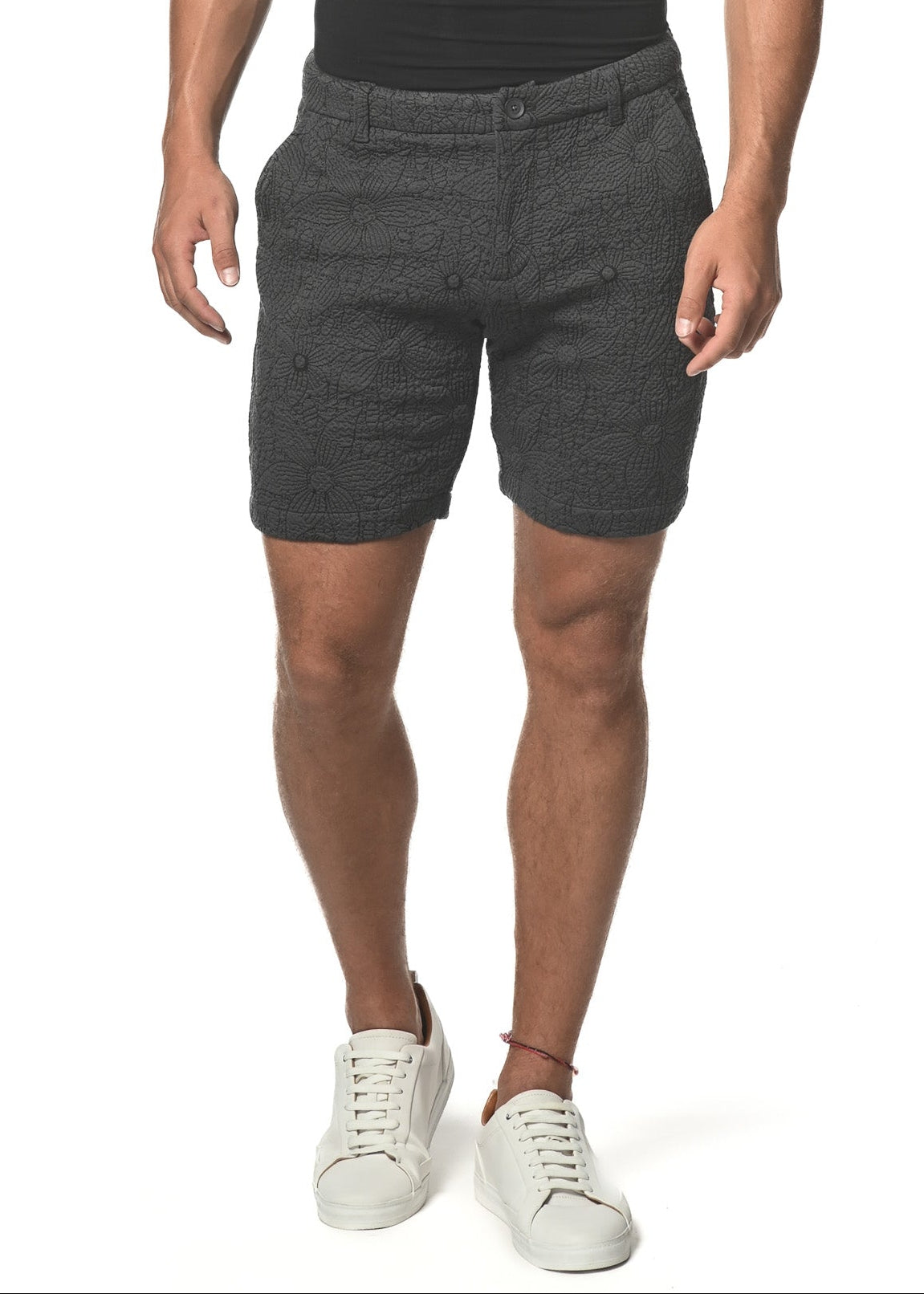 A man wearing charcoal floral print knit shorts and a black V-neck t-shirt, standing against a white background.