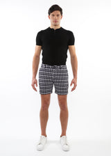 Man wearing a black polo shirt and houndstooth patterned shorts on a white background