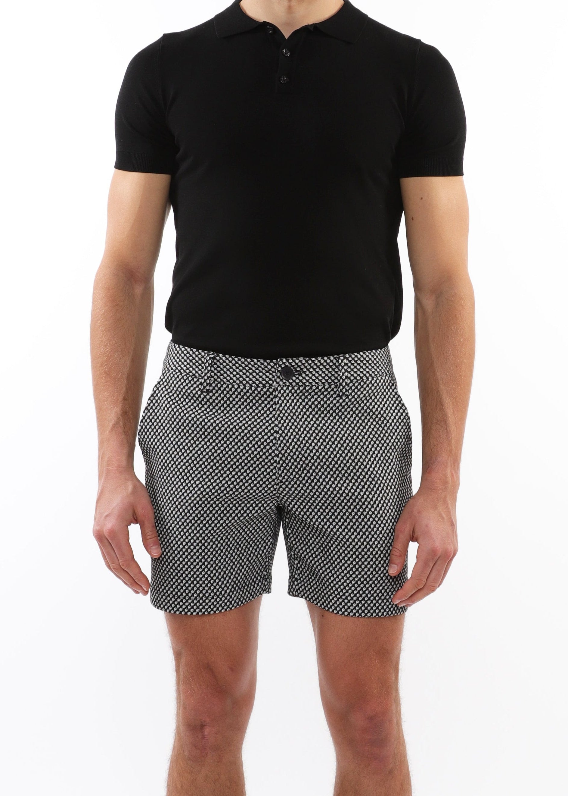 Man wearing a black polo shirt and patterned shorts on a white background