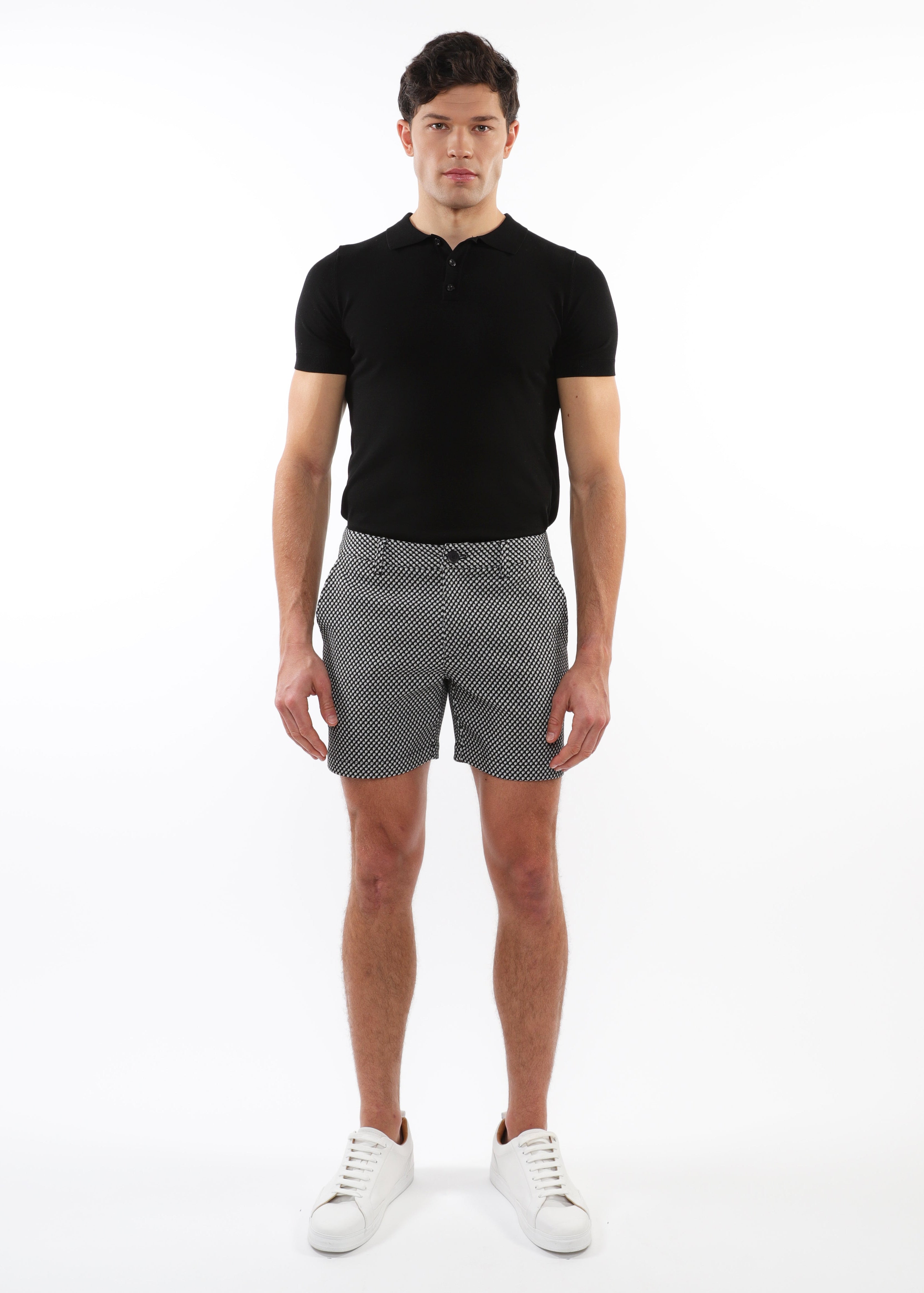 Man wearing a black polo shirt and patterned shorts on a white background