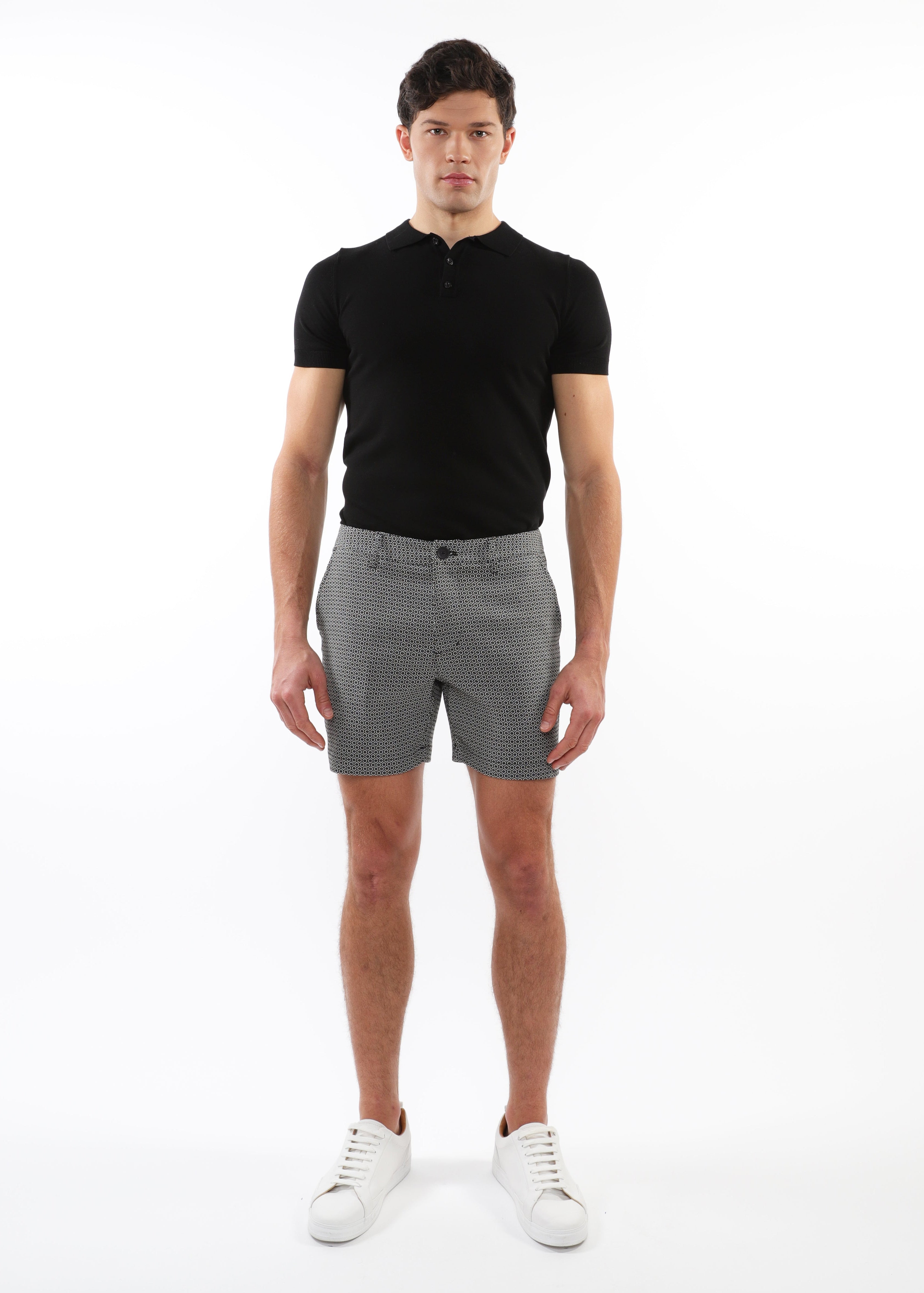 Man wearing a black polo shirt and gray patterned shorts on a white background