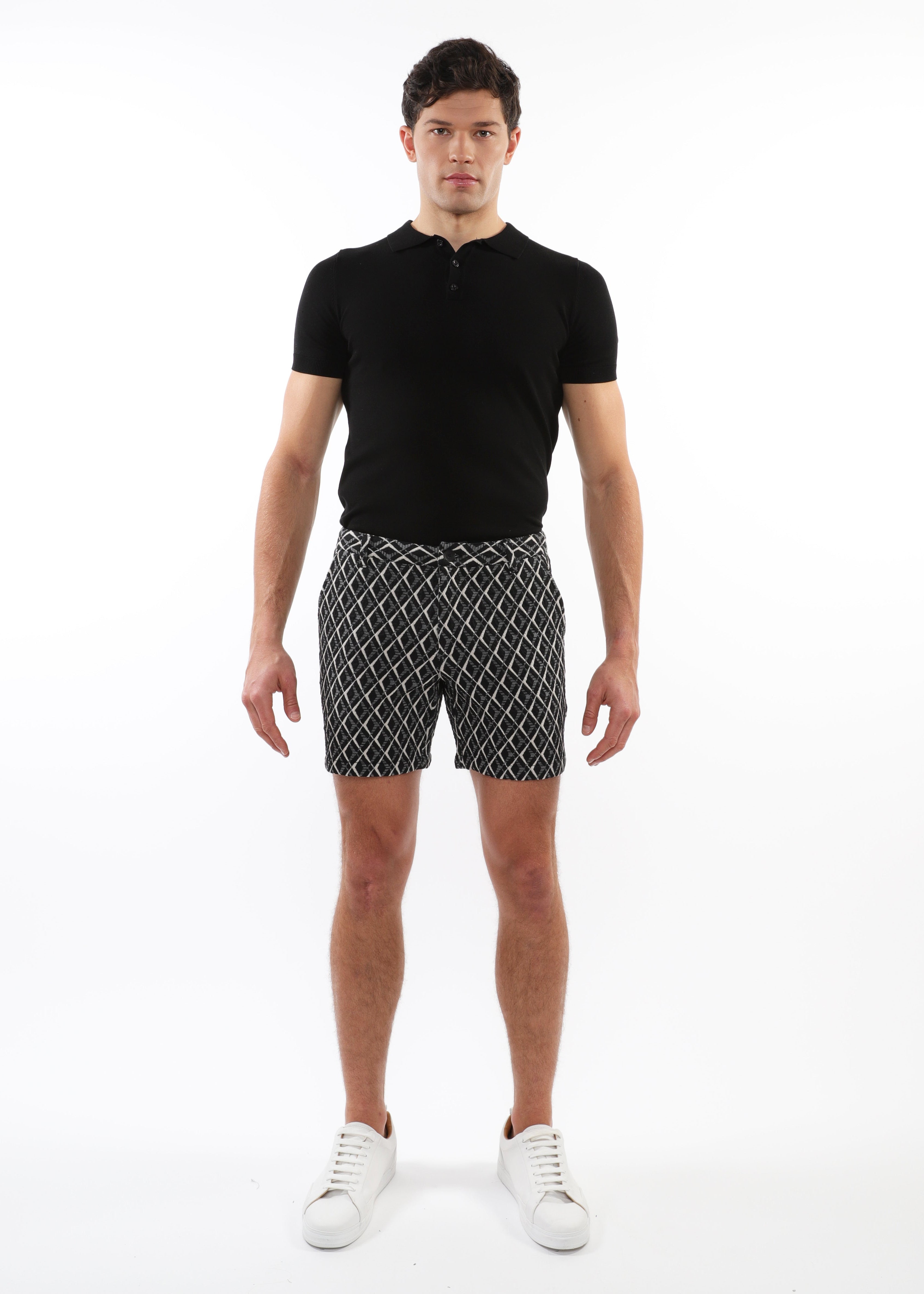 Man wearing a black polo shirt and patterned shorts on a white background