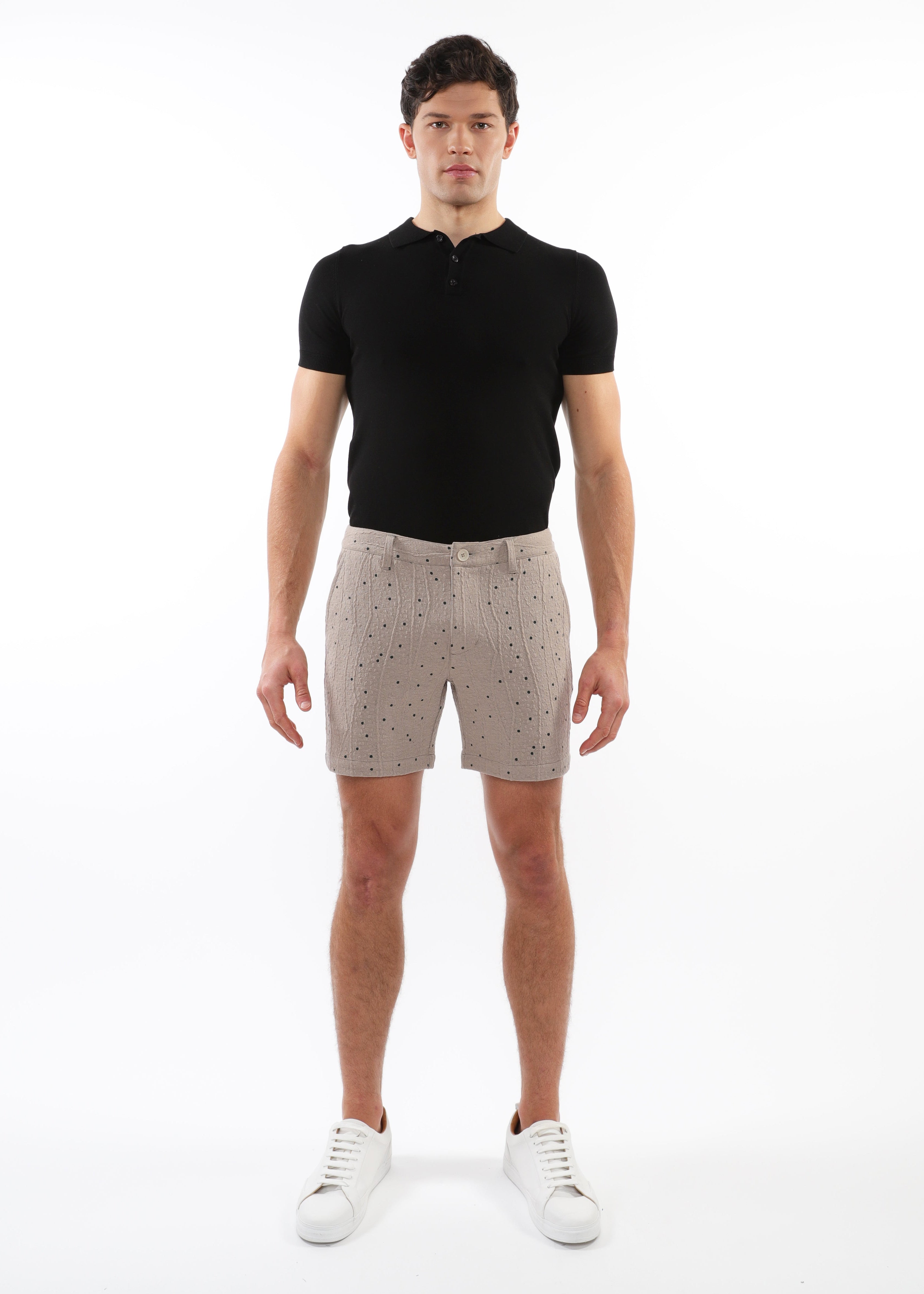Man wearing a black polo shirt and patterned shorts on a white background
